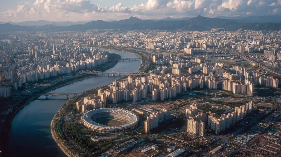 Aerial view of Seoul during the 1988 Seoul Olympics era, featuring the Han River, Olympic Stadium, modern infrastructure and expanding urban skyline in South Korea.