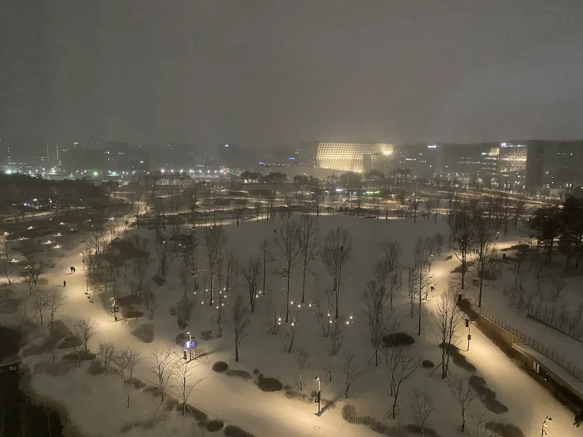 Snowy winter street in Seoul at night with warm lights, pedestrians, and apartment buildings during winter 2026