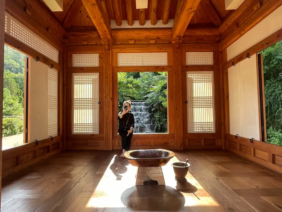 Hanok interior of Cheongun Literature Library in Seoul with wooden beams, open windows, greenery, and a small waterfall outside