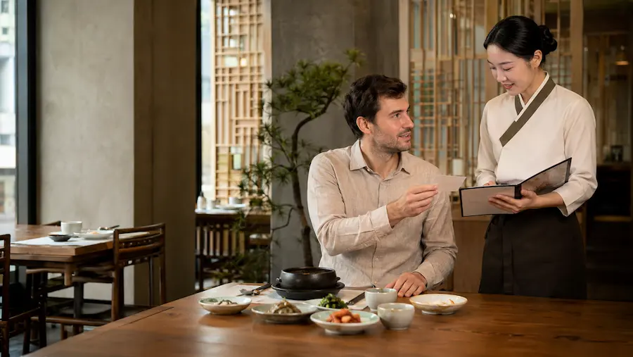 Traveller showing a food allergy card to restaurant staff in Korea before ordering