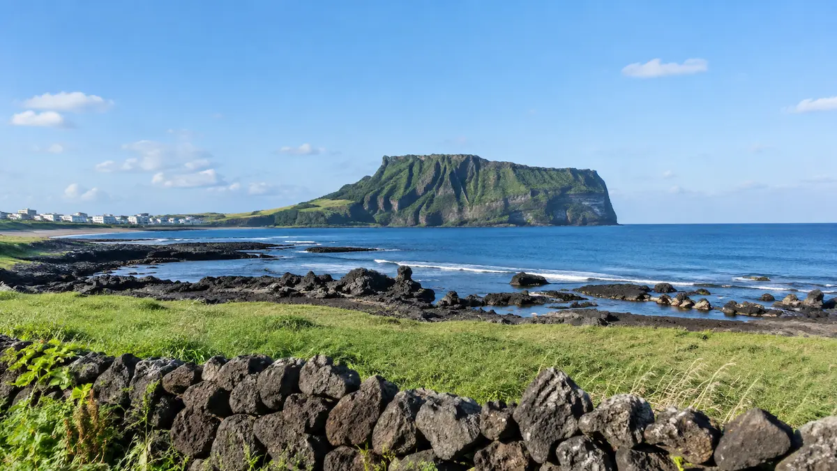 Jeju volcanic coastline with Seongsan Ilchulbong, blue sea and black stone wall